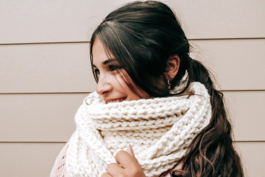 A picture of a girl wearing a cream colour crochet infinity scarf with a plain background