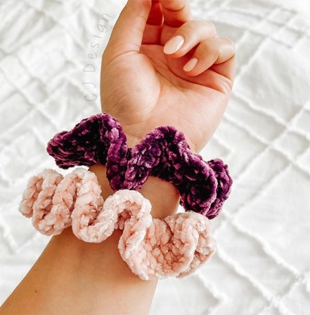 A picture of two crochet scrunchies on a wrist with a white and texture background.