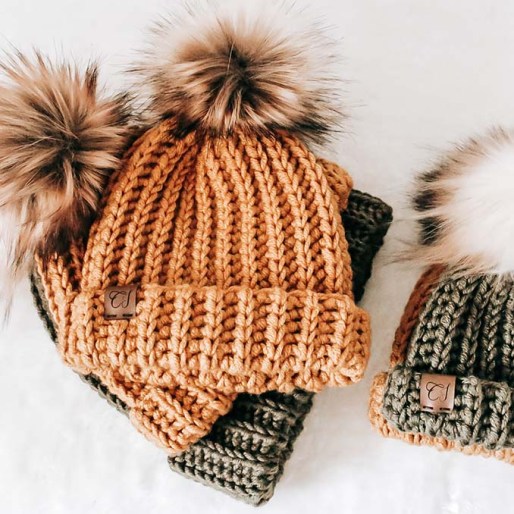 a picture of crochet beanies with faux fur pompoms. 2 yellow/orange colour and 2 olive green on a white surface.